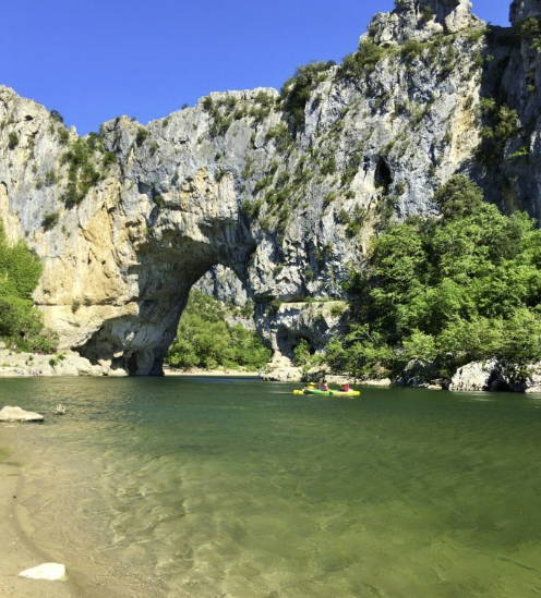 Natural stone arch above turquoise river in the Ardèche Gorge, with kayakers passing underneath